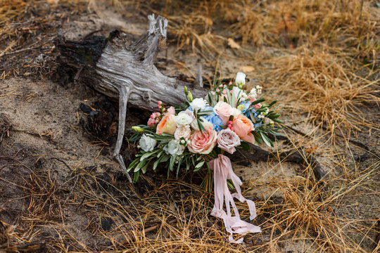 A delicate and very beautiful wedding bouquet of roses, greenery, eustoma and hydrangea on a background of dry stump. Bridal trendy florists in pastel colors. Handle decorated with pink ribbons