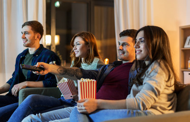 friendship and leisure concept - friends with popcorn and remote control watching tv at home at night