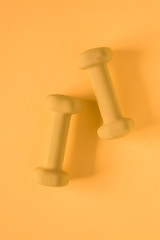 Fitness equipment with womens yellow weights/ dumbbells isolated on a yellow background with copyspace
