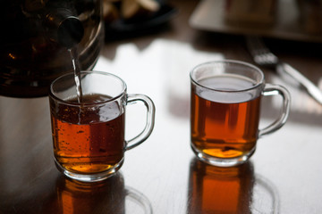 Black hot tea to glass mugs. Selective focus. Close up.