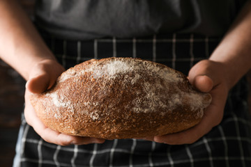 Male hands hold wheat bread against wooden background, space for text Male hands hold wheat bread against wooden background, space for text
