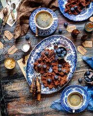 Overhead shot of homemade yummy chocolate waffles on vintage plates with blue ornament stands on wooden dark table