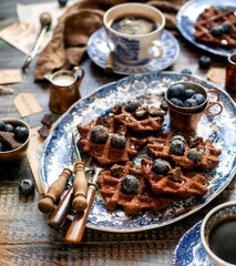 Homemade yummy chocolate waffles on vintage plates with blue ornament stands on wooden dark table
