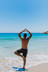 Junger sportlicher Mann macht Yoga am Strand von Paros auf den Kykladen in Griechenland und macht ein Herz mit den FIngern