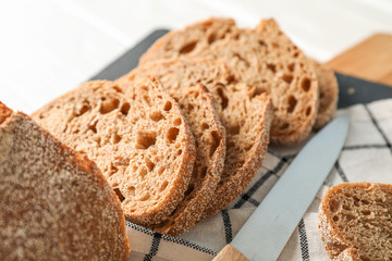 Composition with bread, knife, kitchen towel and cutting board on white wooden background