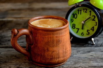 Home coffee with milk in a ceramic cup, in the early morning. Alarm clock.