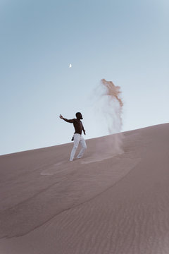 A young black man jumping in dunes of sand at night