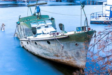 Sunken ship at the edge of a frozen river on a sunny winter day