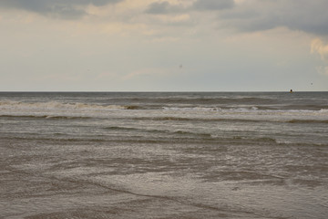 Fototapeta na wymiar Plażą nad morzem w pochmurny dzień pod niebem z chmurami.