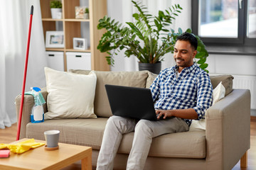 household, housework and technology concept - indian man with laptop computer, mop and bucket after home cleaning