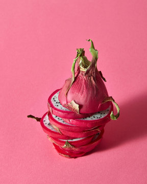 A dragon fruit or Pitaya cut into slices made up on a pink backg