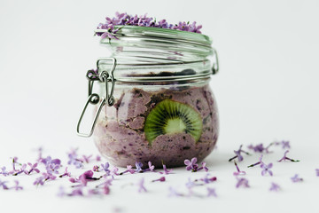 Purple healthy smoothie breakfast in a glass jar with lilac flowers