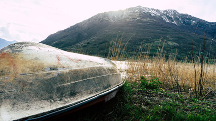 Small white boat turned upside down with dirty bottom and keel on seaside with sea and mountains at...