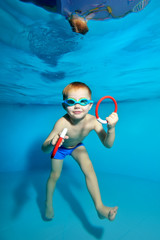 A little boy goes in for sports and swims underwater in the pool near the water surface. Portrait. Underwater photography. Blue background. Vertical orientation © alexbard