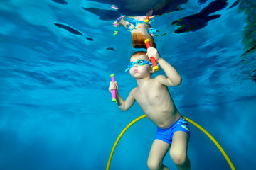 A little boy goes in for sports and swims underwater in the pool. Floating with toys in his hands. Portrait. Close up. Underwater photography. Horizontal orientation © alexbard