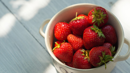 Ripe strawberries in a bowl on the white wooden table