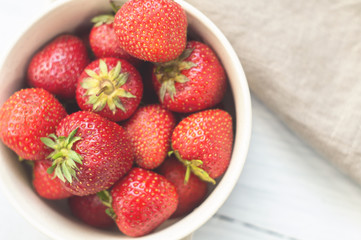 Ripe strawberries in a bowl on the white wooden table