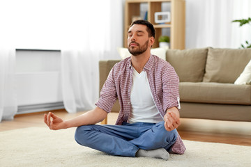 mindfulness, meditation and relaxation concept - man meditating in lotus pose at home