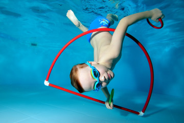 A little boy is playing fun, tumbling underwater at the bottom of the pool. Dancing underwater. Creative. Open his eyes. Portrait. Underwater photography. Horizontal orientation of the image - obrazy, fototapety, plakaty
