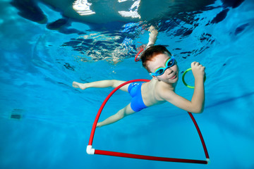 Sporty little boy, swim out of the red Hoop under the water in the pool with toys in his hands....