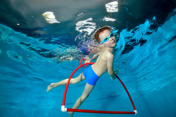 A little sports boy swims under water in the pool, emerges to the surface of the hula Hoop and looks at the camera. Portrait. Underwater photography. Horizontal orientation © alexbard