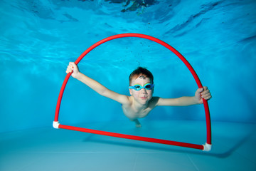 Smiling little sports boy, engaged in swimming in the pool, underwater at the bottom, posing with a...
