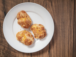 Three cream puffs on a white plate filled with custard and topped with sweet syrup. Close up.