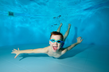 Happy sporty boy swimming underwater, smiling mouth wide, scream, . Posing for the camera with his eyes open. Portrait. Photo underwater. Horizontal orientation © alexbard