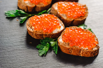 Red caviar on bread on slate background.