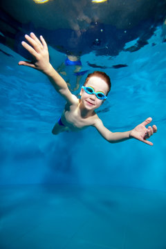 A small sports a boy he was smiling is sailing under's surface water. Creative. Posing with open eyes. Portrait. Underwater photography. Vertical orientation of the image