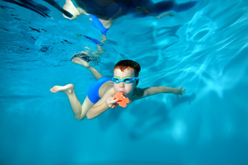 Little sports boy swimming underwater in the pool, posing with a toy in his hands and looking at...