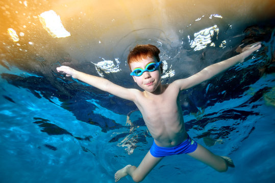 A little boy swims and plays underwater in the pool with his hands spread apart and looks at the camera. Portrait. Underwater photography. Horizontal orientation of the image