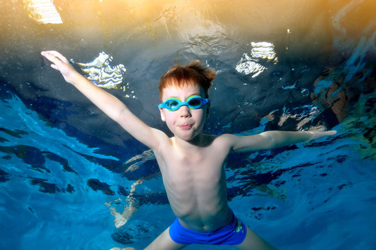 A little boy is swimming underwater in the pool with his arms outstretched. Dancing underwater. Creative. Portrait. Underwater photography. Horizontal orientation of the image