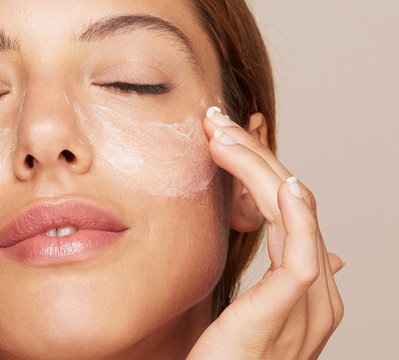 Woman portrait applying cream or moisturiser isolated In studio - skin care hydration closeup