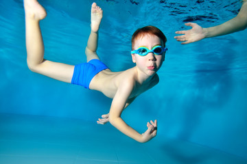 A happy little boy goes in for sports and swims underwater in the pool with his arms outstretched....