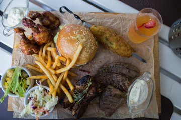 Food plate with fried chicken wings, burger, fried potatoes, sauce, salad, grilled meat . Fast unhealthy tasty food concept