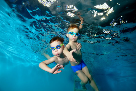 Two beautiful sports little boys swim, frolic, dance under the surface of the water in the pool, on a blue background. View from the bottom of the pool. Portrait. Underwater photography