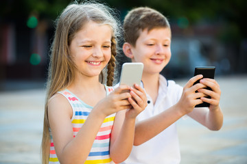smiling girl and boy looking at mobile phones in park