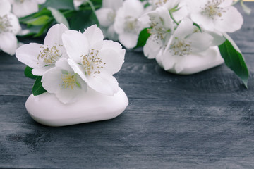 Obraz na płótnie Canvas Cosmetic soap and white jasmine flowers with green leaves lie on a wooden background. There is a place for your text.