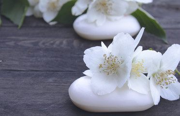 Cosmetic soap and white jasmine flowers with green leaves lie on a wooden background. There is a place for your text.