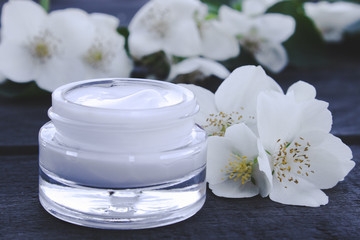Fototapeta na wymiar Cosmetic cream in a glass jar with jasmine flowers on a wooden background.