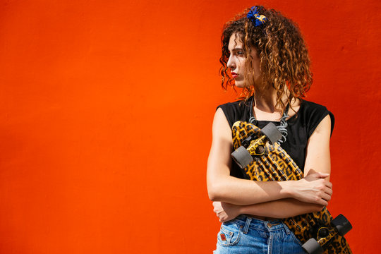 Young girl portrait with skateboard on red orange wall