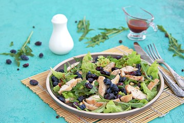 Light salad with arugula, lettuce, grilled chicken and honeysuckle on a brown plate on a turquoise background. Healthy food, diet. Selective focus