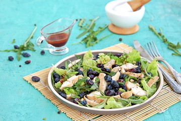 Light salad with arugula, lettuce, grilled chicken and honeysuckle on a brown plate on a turquoise background. Healthy food, diet. Selective focus