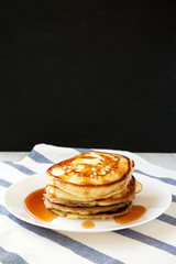Side view, homemade pancakes with butter and maple syrup on a white plate.