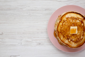Homemade pancakes with butter and maple syrup on a pink plate, top view. Overhead, flat lay, from above. Space for text.