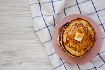 Homemade pancakes with butter and maple syrup on a pink plate, top view. Flat lay, overhead, from above. Copy space.