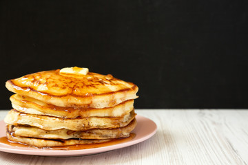 Homemade pancakes with butter and maple syrup on a pink plate, side view. Copy space.