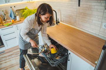 young pretty woman putting dishes in dishwasher