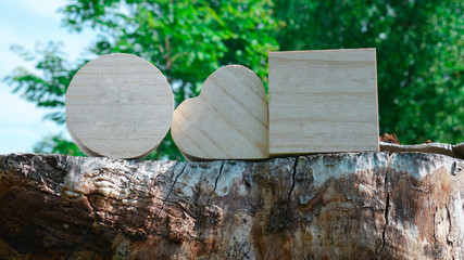Wooden closed boxes in the shape of a cube, heart and circle on stump - green trees in the background